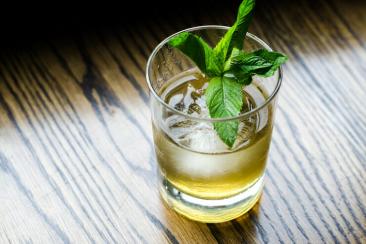 a whiskey cocktail garnished with mint leaves sitting on a wooden table