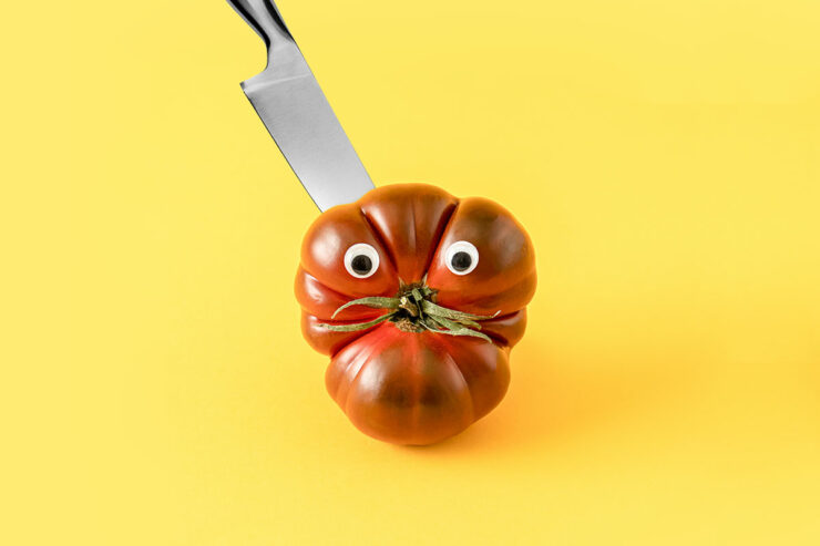 odd shaped tomato with google eyes with knife sticking out