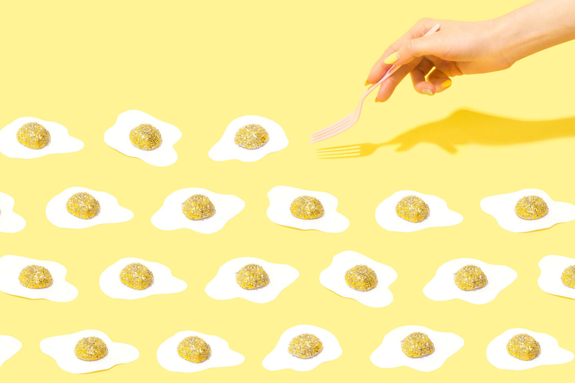 a manicured hand with a fork trying to pick up one of many sparkly eggs