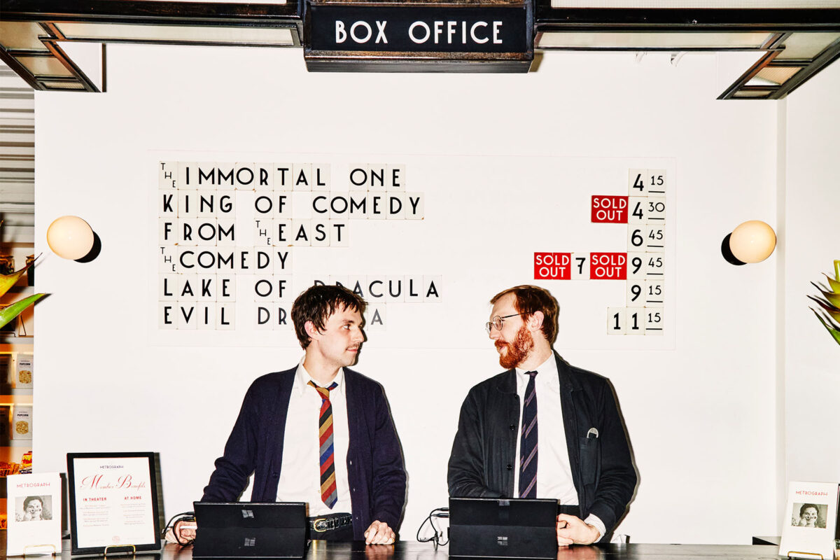 two men standing behind the counter of a vintage box office