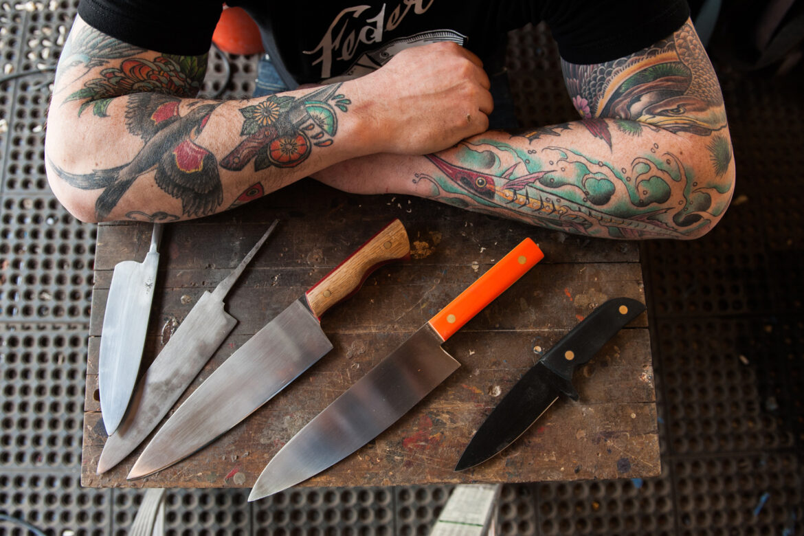 knives displayed in front of crossed tattooed arms