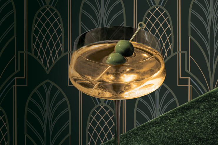 an aquavit martini with two olives against an art deco pineapple patterned background